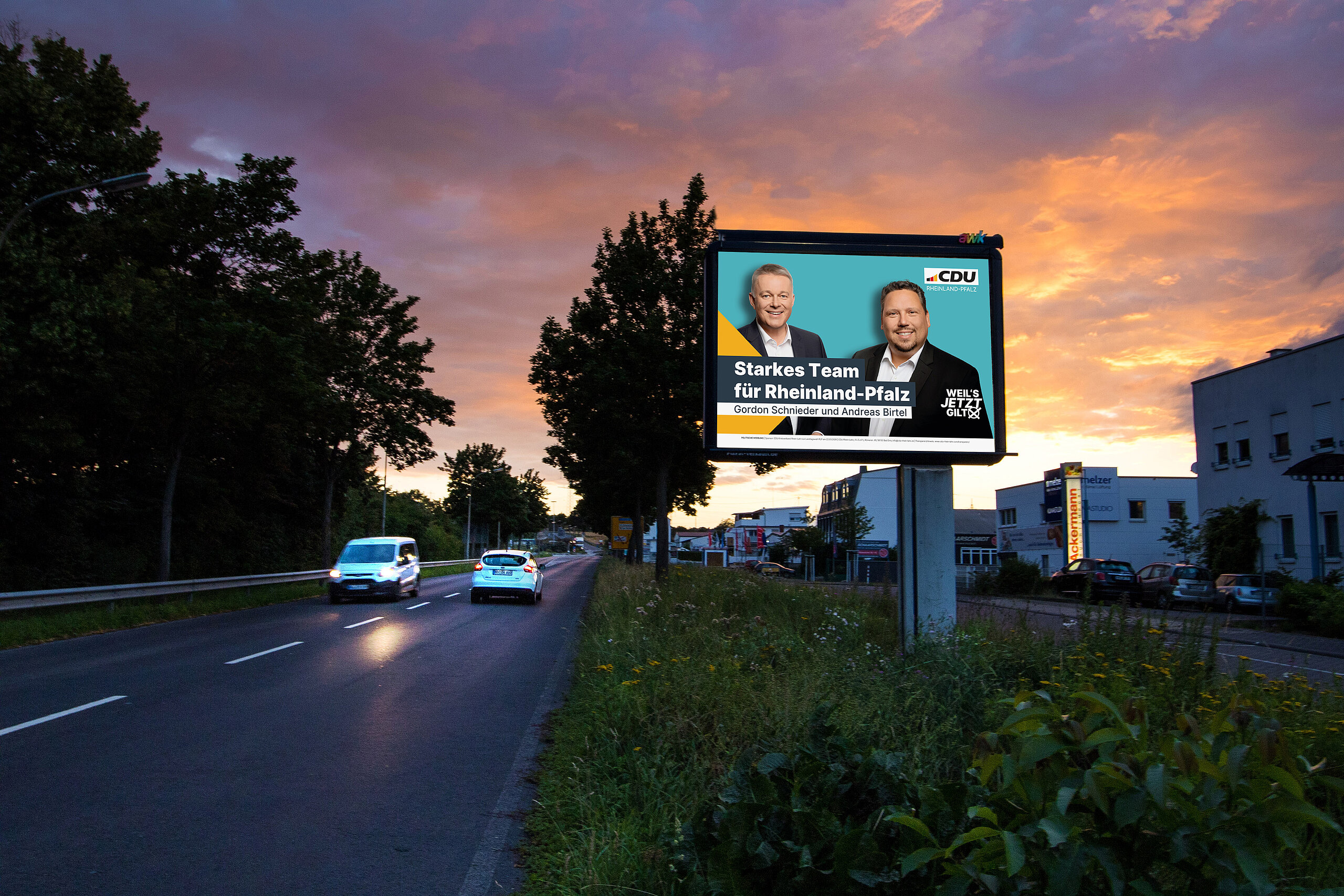 Wahlkampagne-Plakat der CDU an befahrener Straße bei Sonnenuntergang: Zwei Männer im Anzug. Überschrift: "Starkes Team für Rheinland-Pfalz."