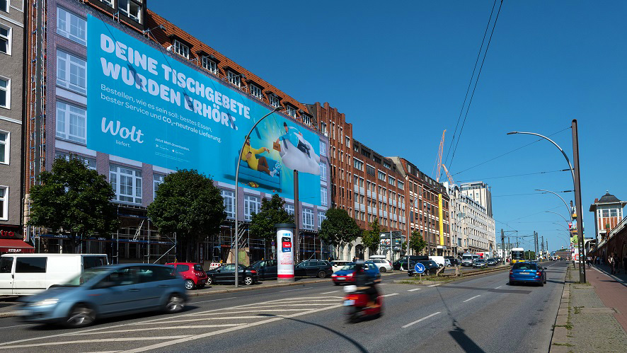 Riesenposter von Wolt auf einem Gebäude in der Stadt, mit einer Werbung für schnelle, CO2-neutrale Essenslieferung. XXL-Werbung, die große Aufmerksamkeit erregt.